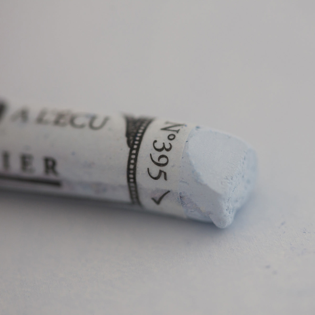 A close-up of a white Sennelier extra soft pastel on the same coloured background, with the colour information printed on the paper wrap.