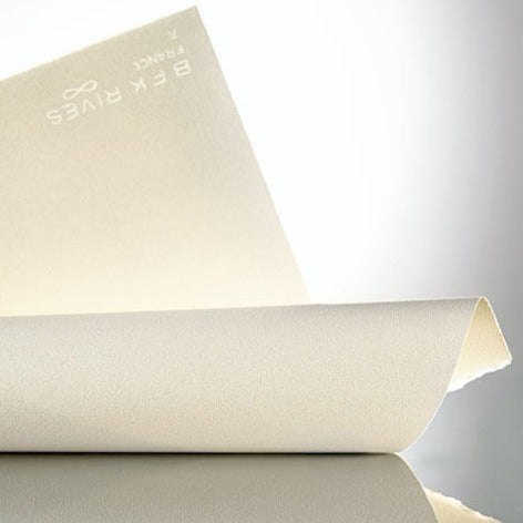 A rolled piece of BFK Rives paper unrolling to show its texture and colour, with a watermark of the brand name and infinity symbol visible on the paper edge.