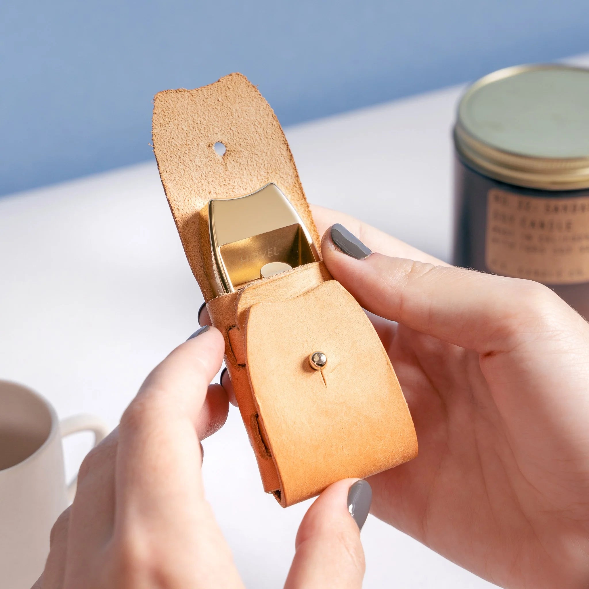 An image if a hovel leather sheath being held with its flap open to show a brass Hovel Pencil Plane visible inside.