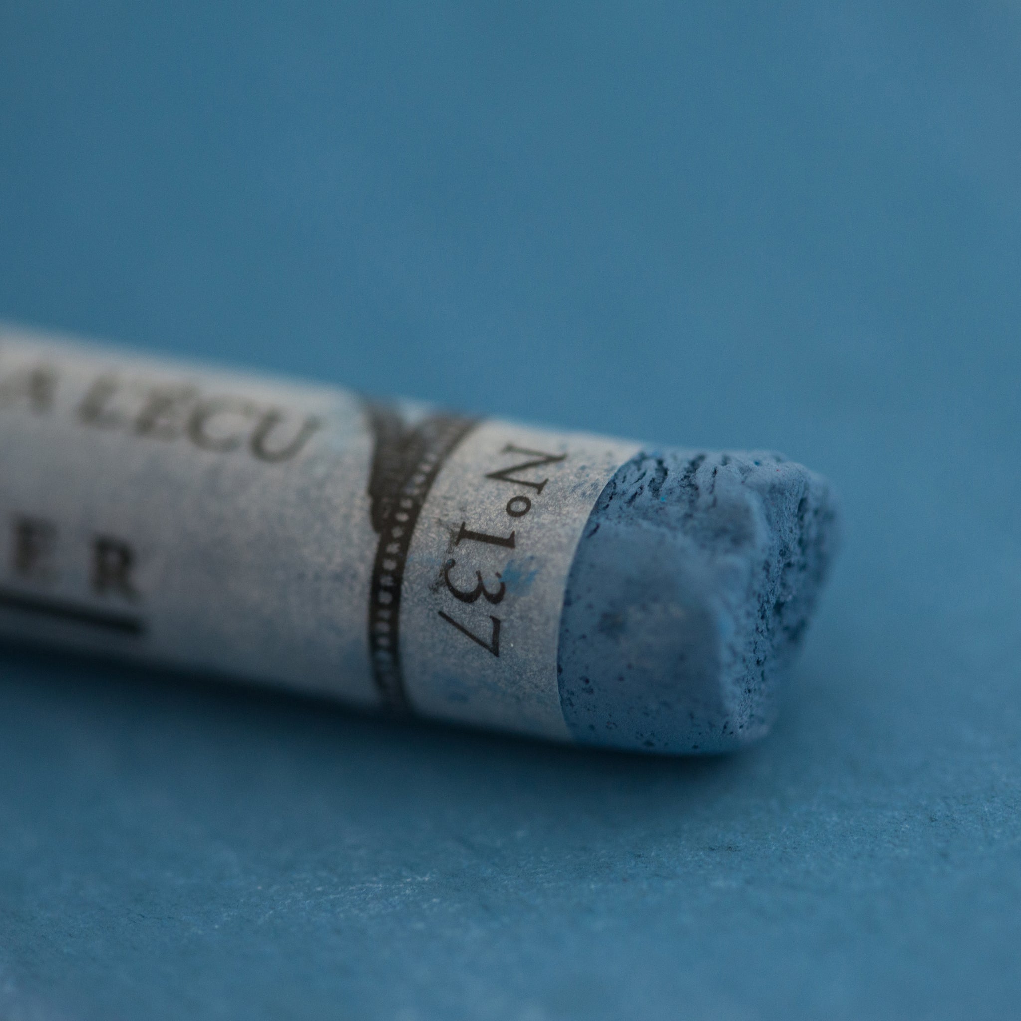 A close-up of a Sennelier large extra soft pastel on a blue background.