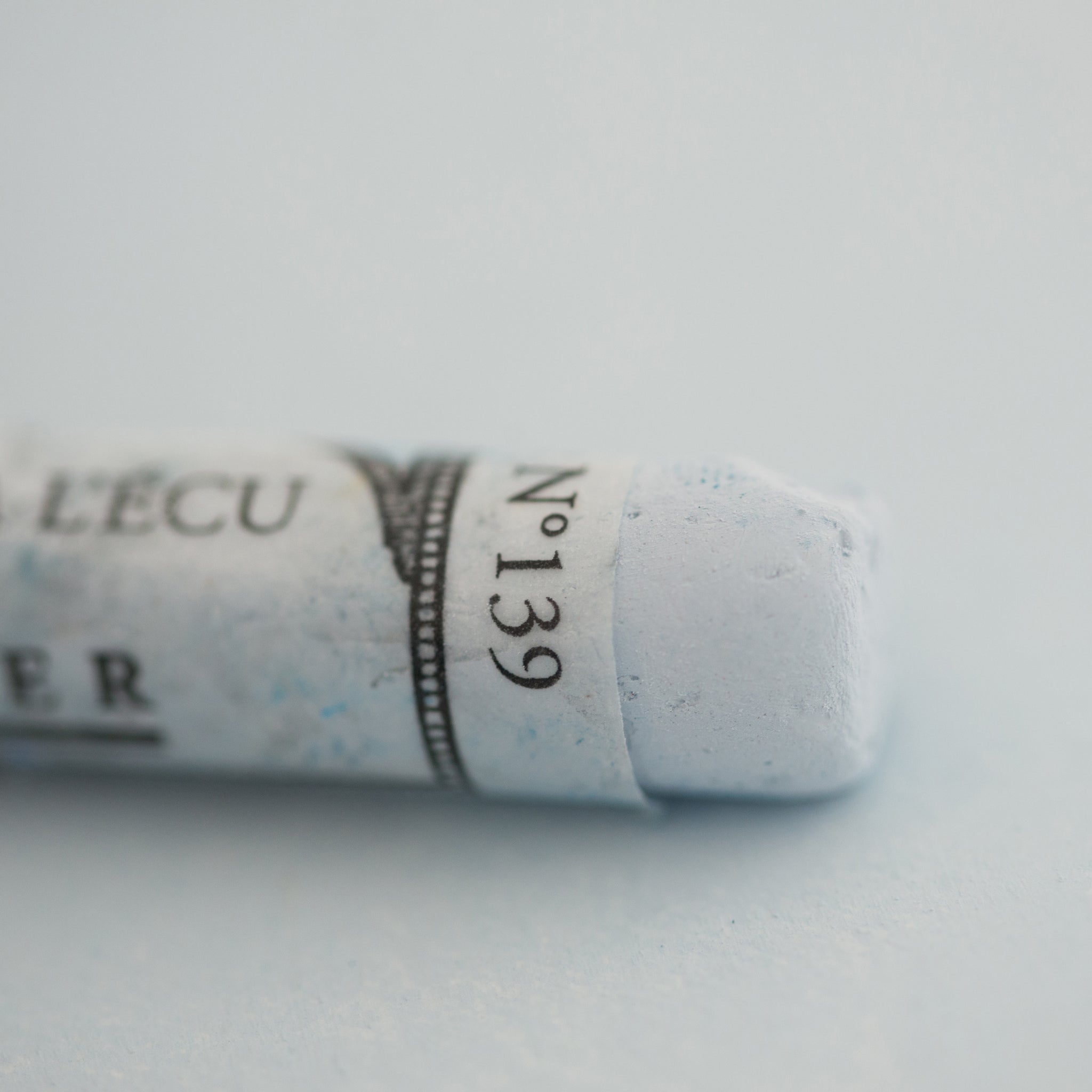 A close-up of a Sennelier large extra soft pastel on a light blue background.