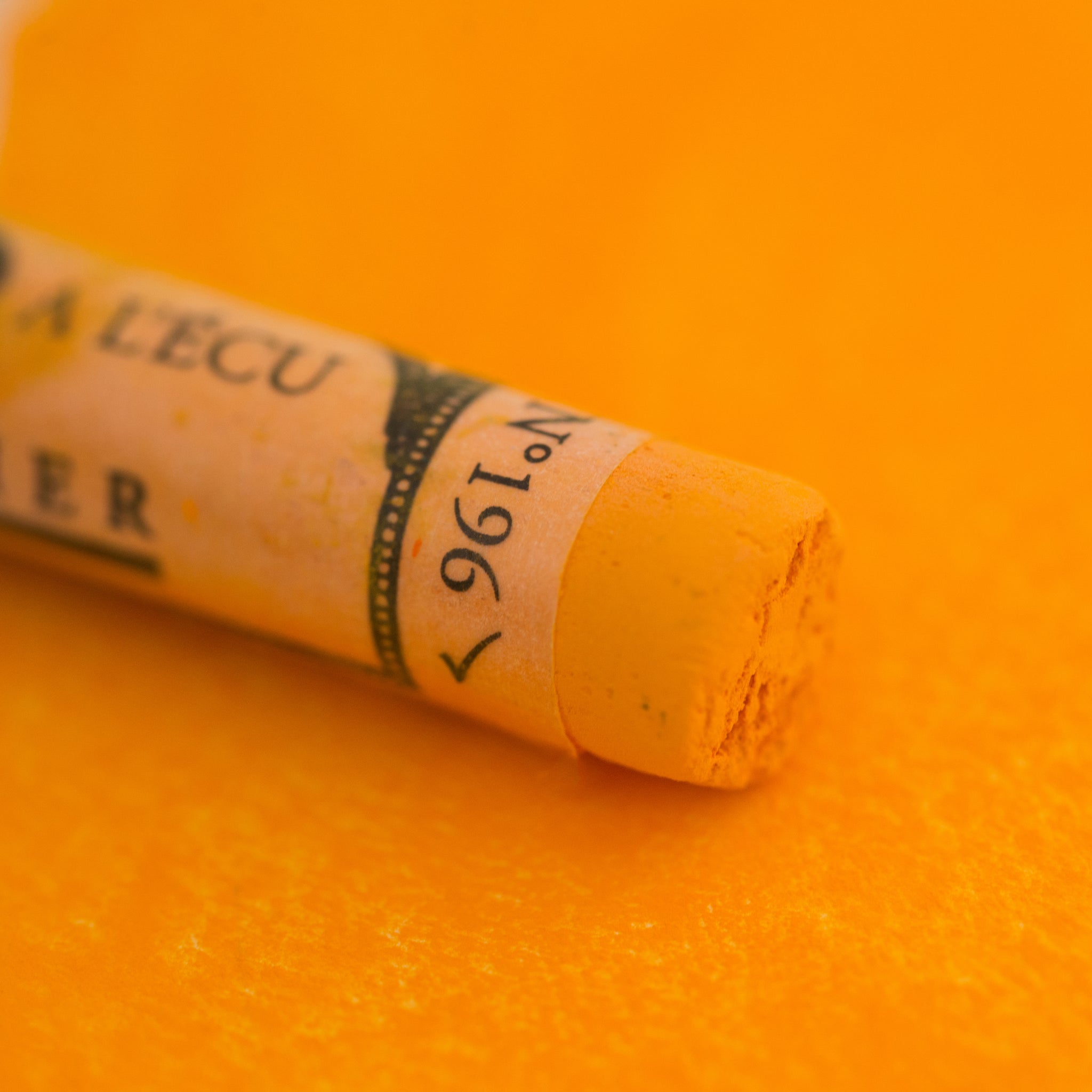 A close-up of a Sennelier large extra soft pastel on an orange background.