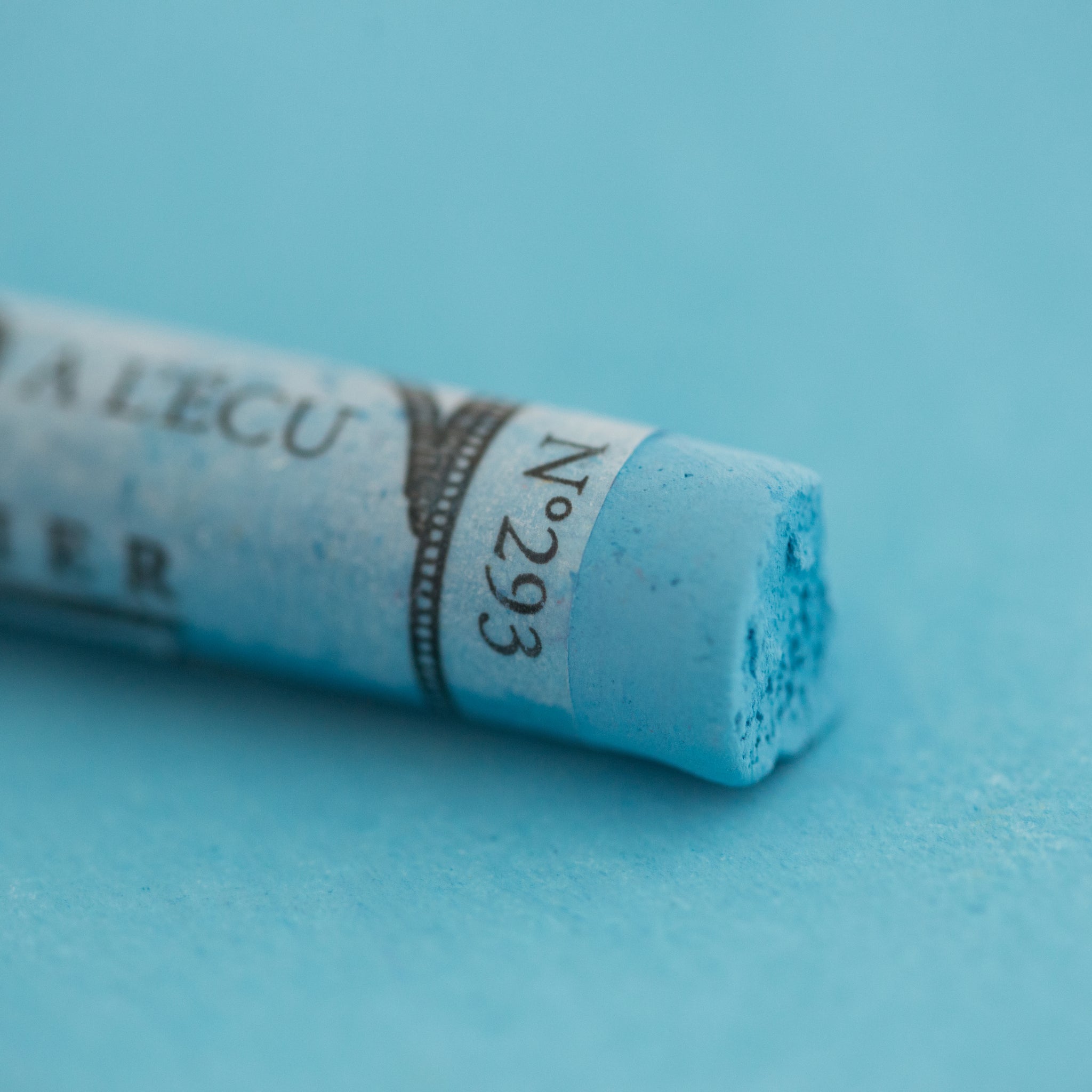 A close-up of a Sennelier large extra soft pastel on a blue background.