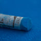A close-up of a Sennelier large extra soft pastel on a blue background.
