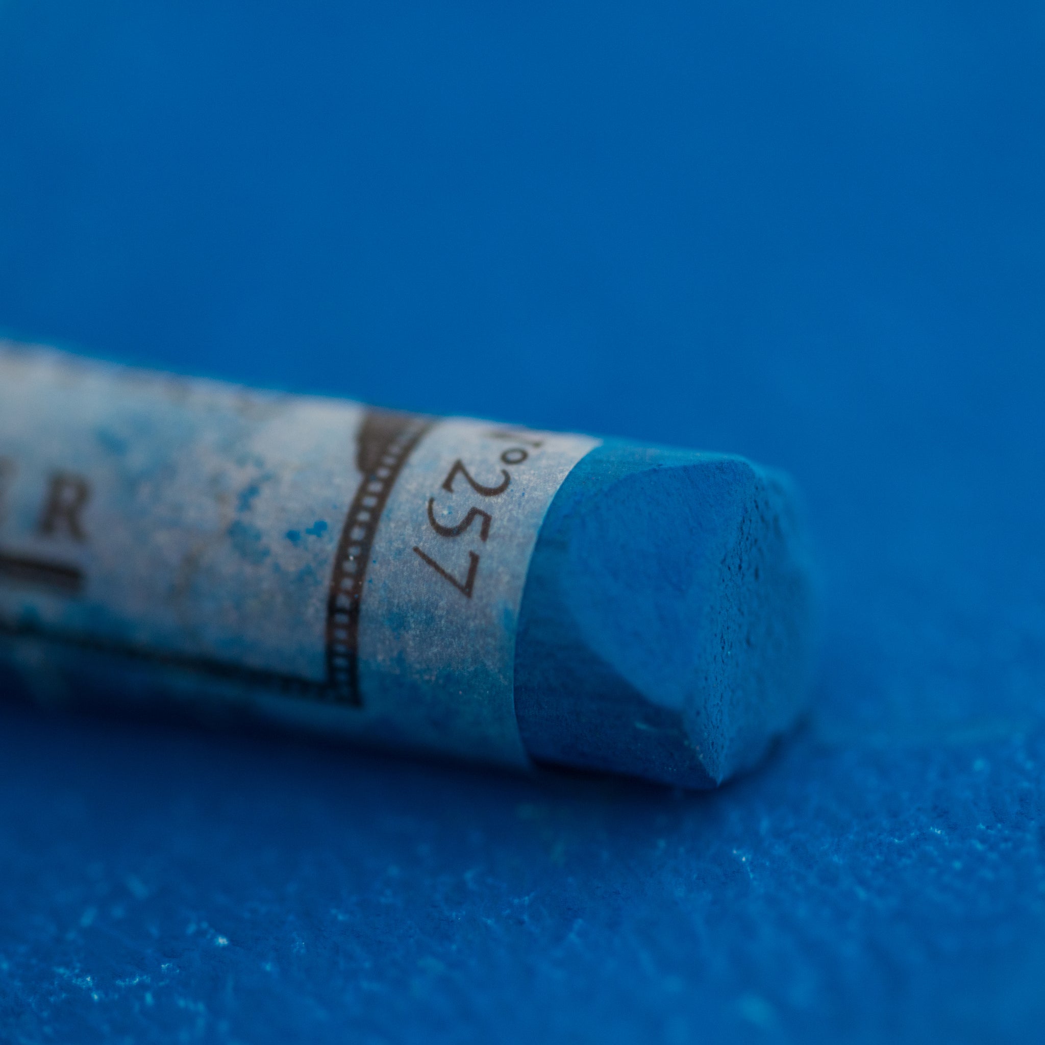 A close-up of a Sennelier large extra soft pastel on a blue background.
