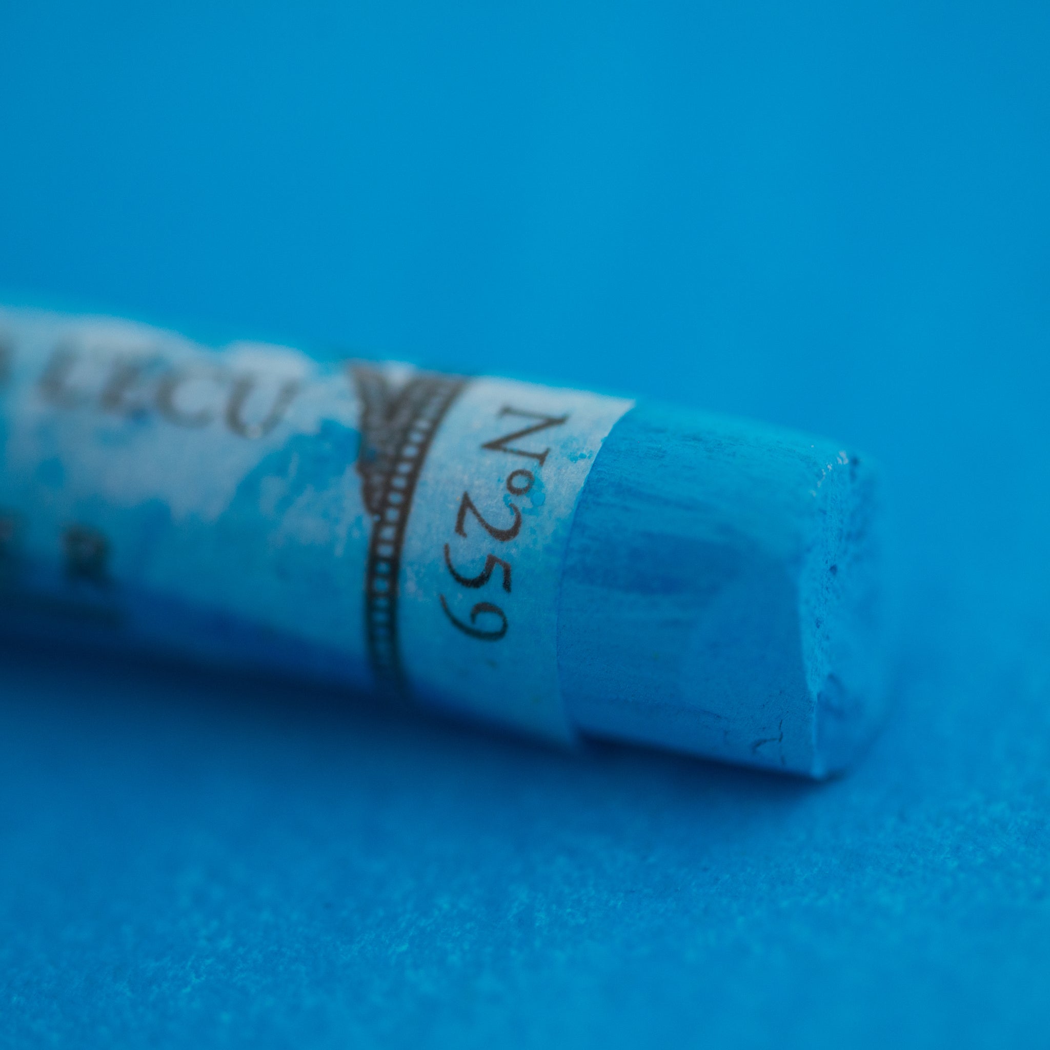 A close-up of a Sennelier large extra soft pastel on a blue background.