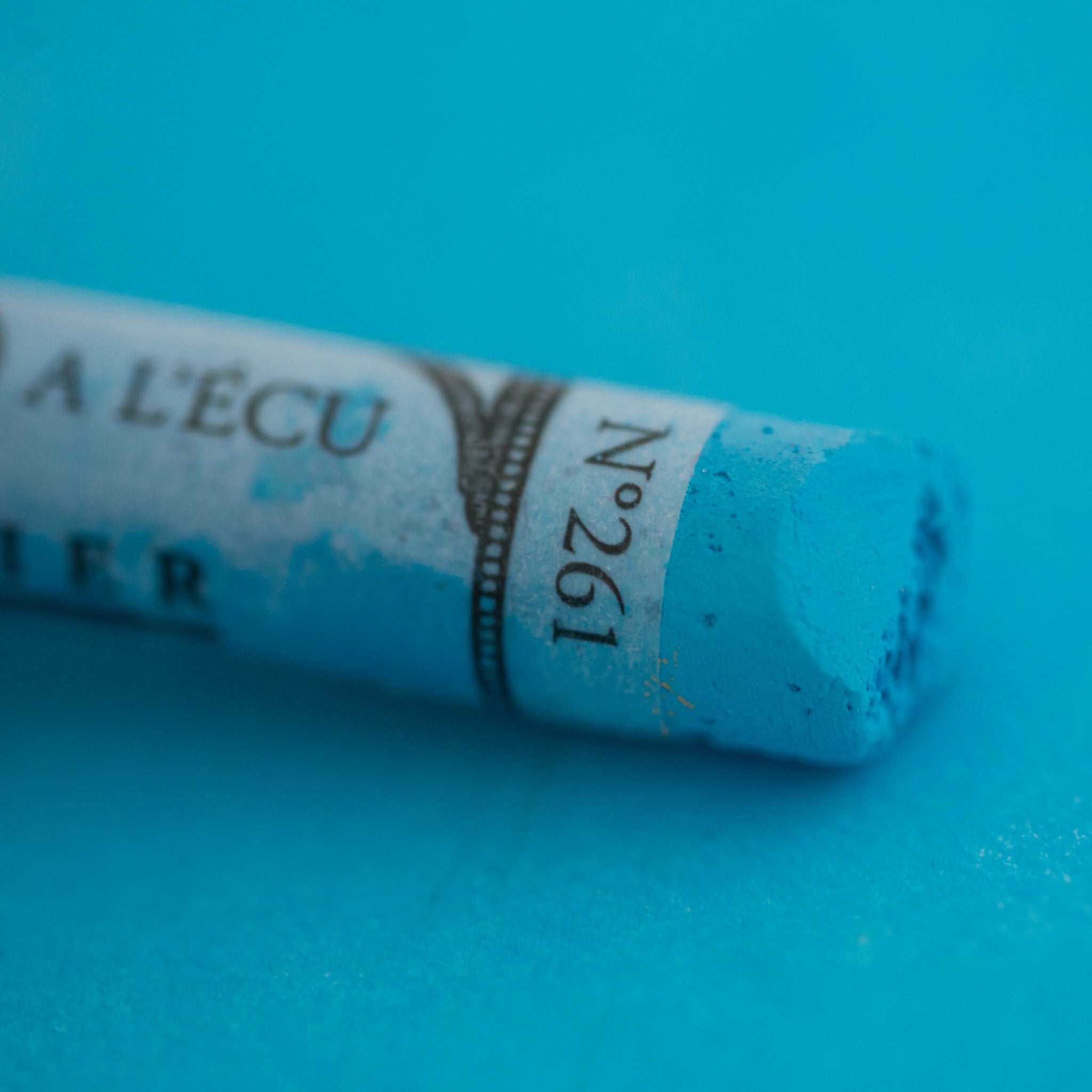 A close-up of a Sennelier large extra soft pastel on a blue background.