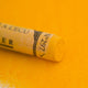 A close-up of a Sennelier large extra soft pastel on a yellow background.