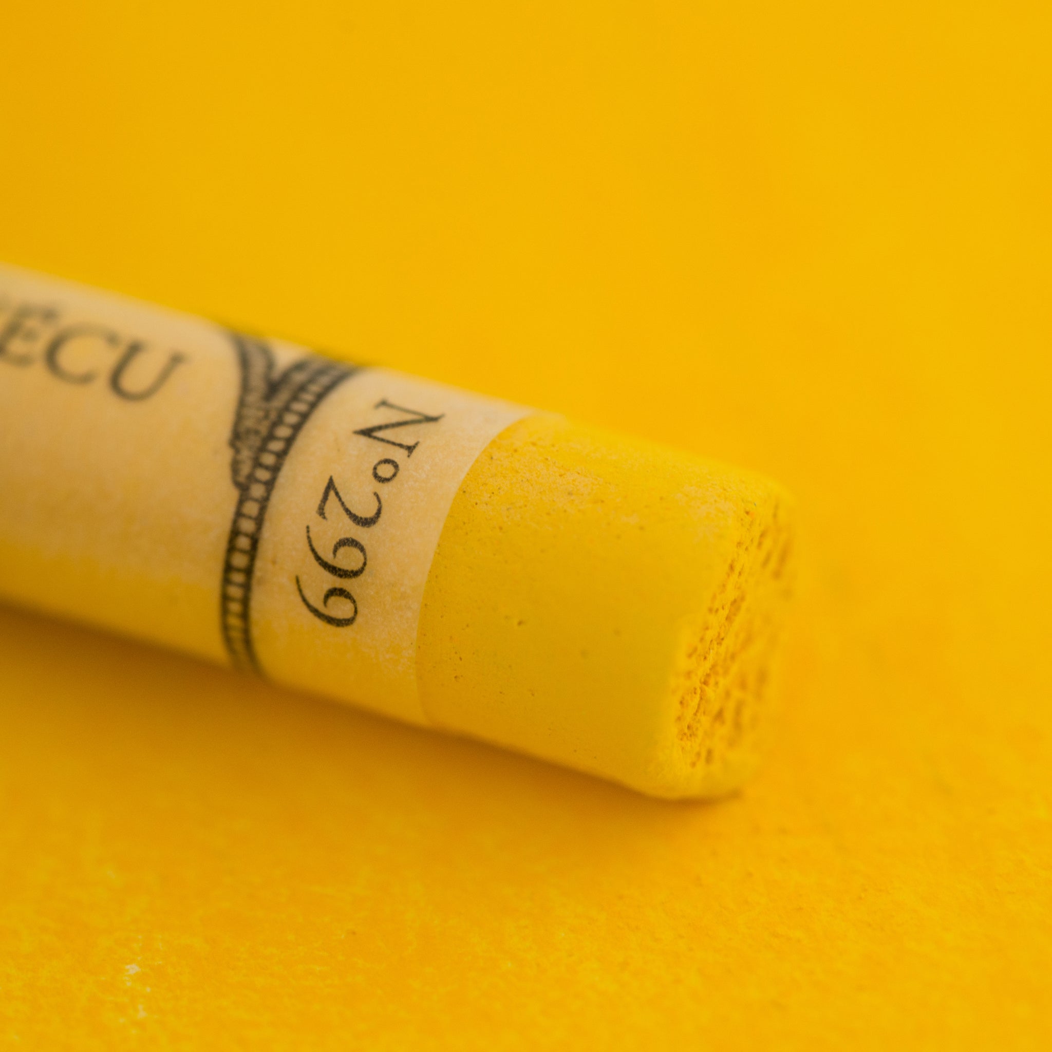 A close-up of a Sennelier large extra soft pastel on a bright yellow background.