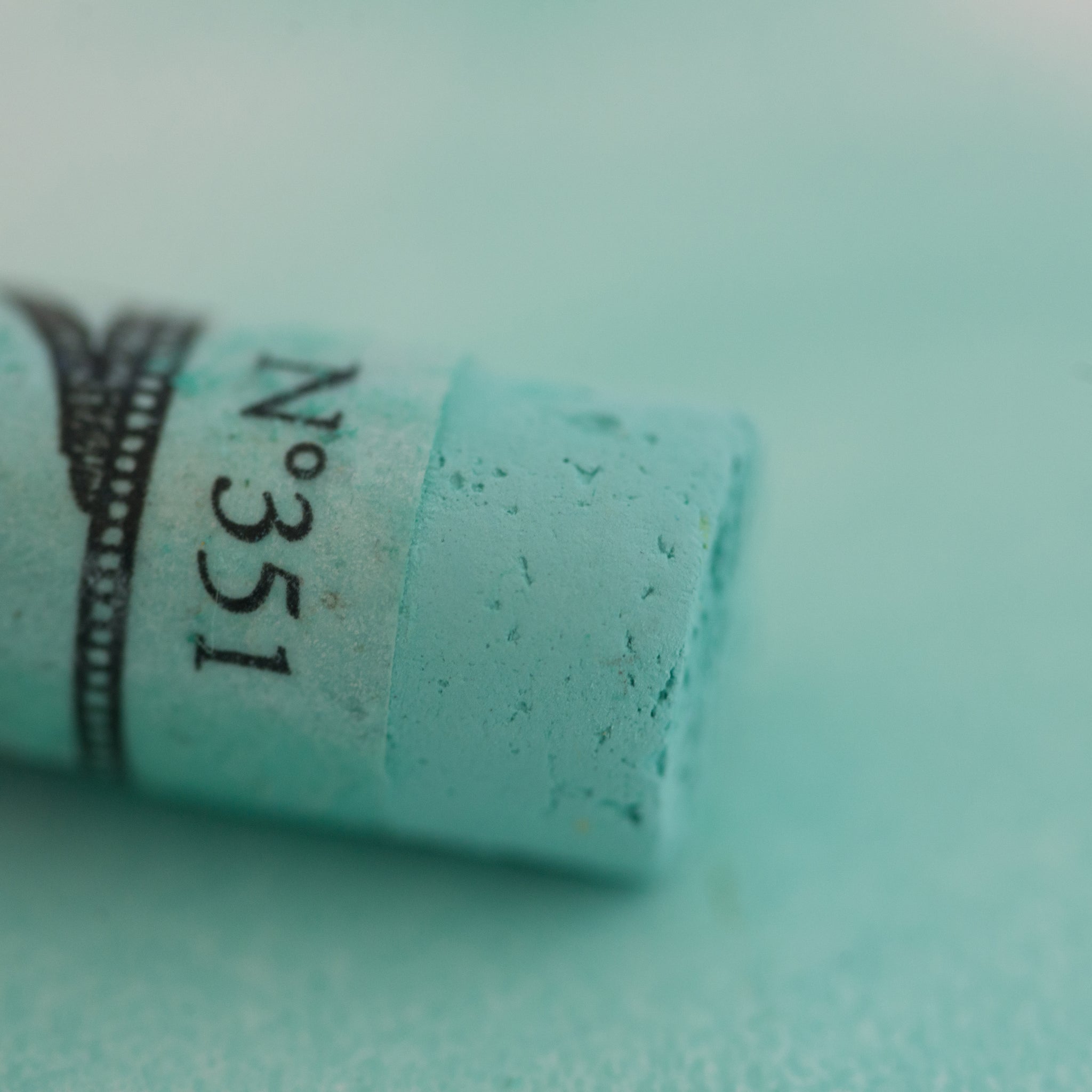 A close-up of a Sennelier large extra soft pastel on a light green background.