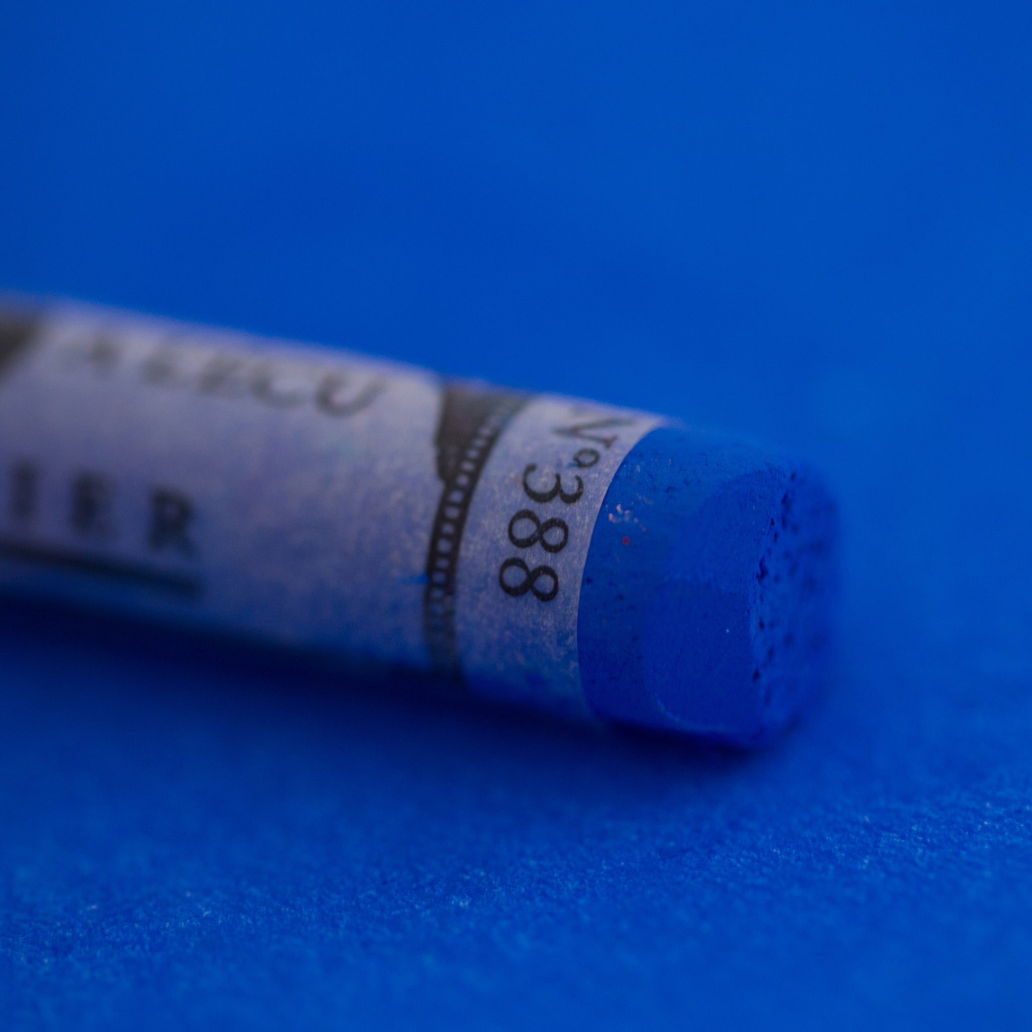 A close-up of a Sennelier large extra soft pastel on a bright blue background.