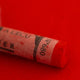 A close-up of a Sennelier large extra soft pastel on a bright red background.