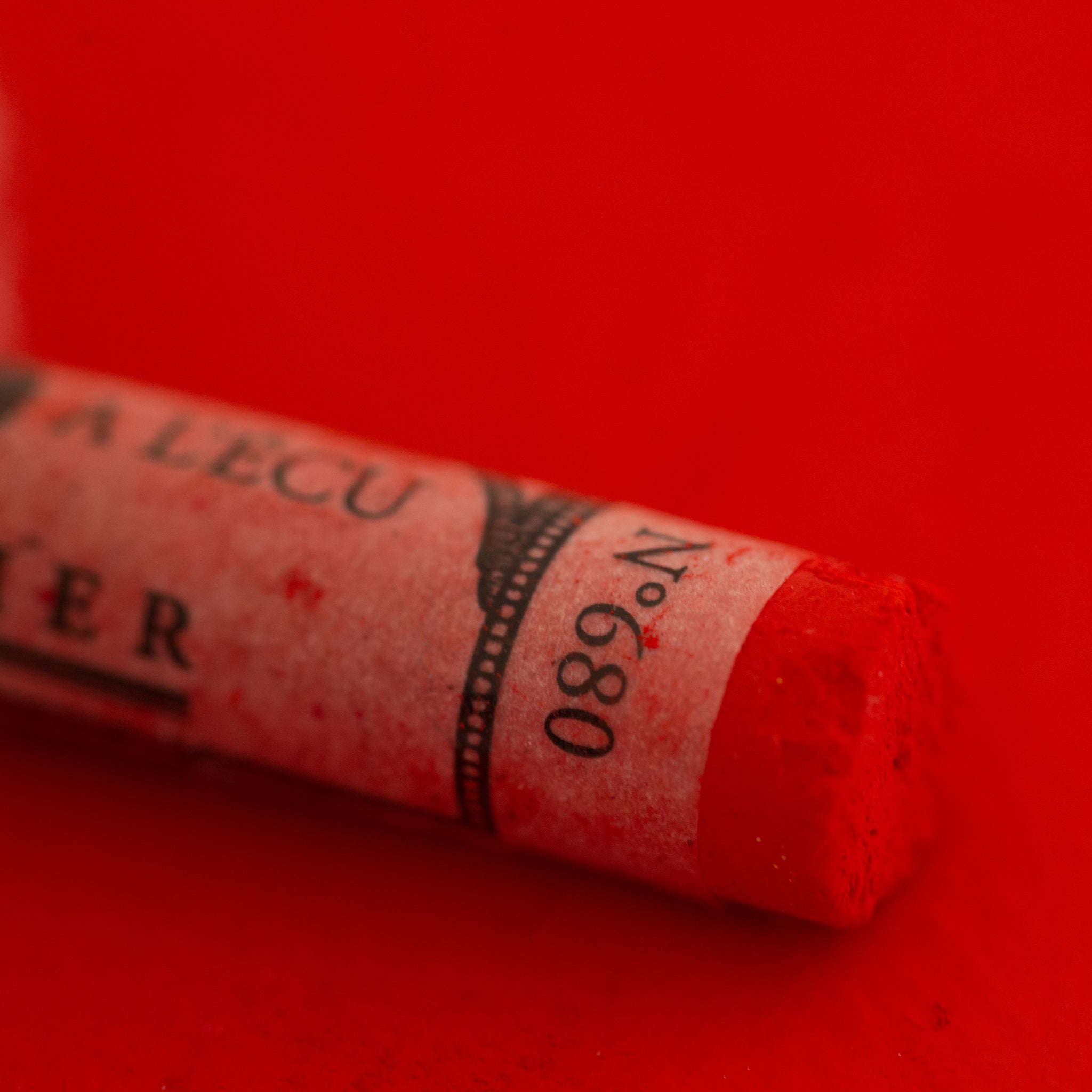 A close-up of a Sennelier large extra soft pastel on a bright red background.