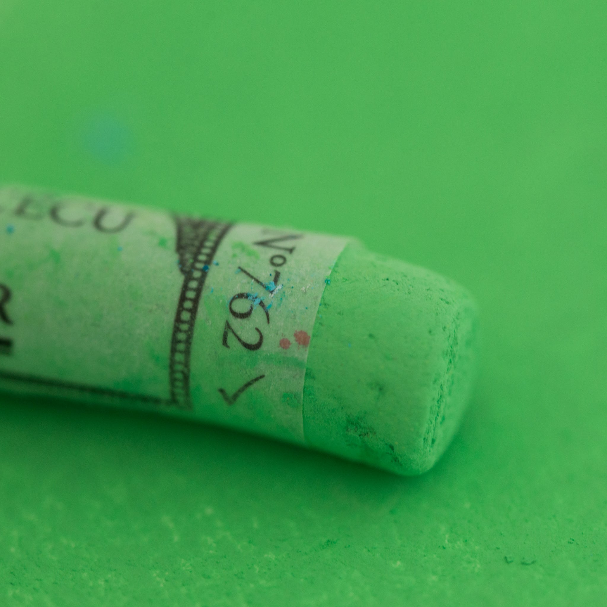 A close-up of a Sennelier large extra soft pastel on a bright green background.