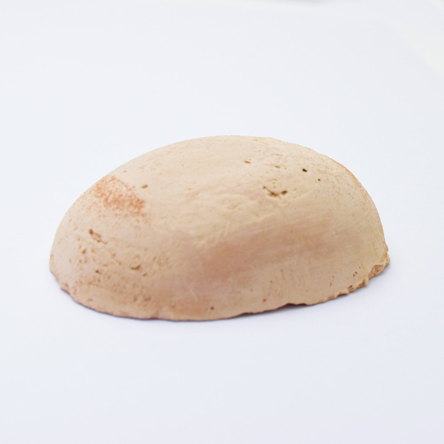 A half egg shaped pastel in a soft pink / ochre tone, sitting on a white background