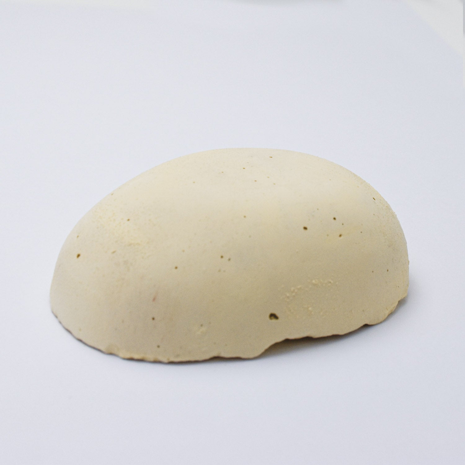 A half egg shaped pastel in a soft yellow  tone, sitting on a white background
