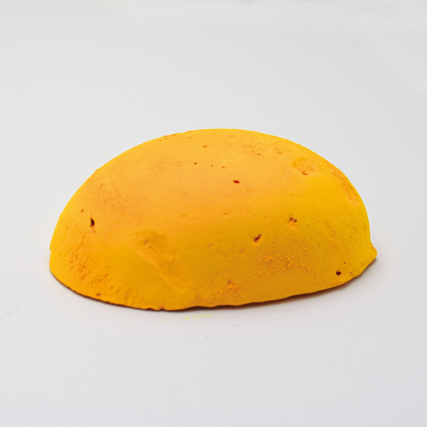 A half egg shaped pastel in a bright warm yellow, sitting on a white background