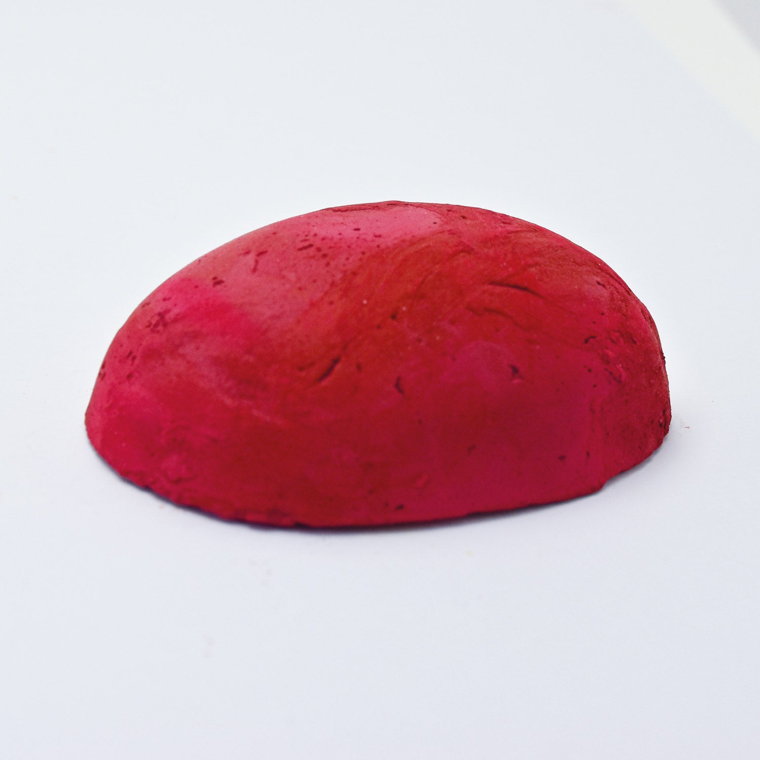 A half egg shaped pastel in a cool red tone, sitting on a white background