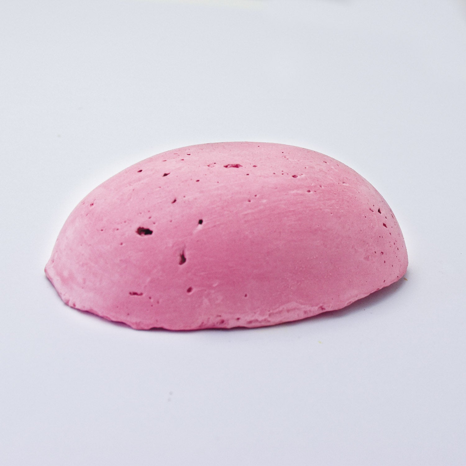 A half egg shaped pastel in a mid-pink tone, sitting on a white background