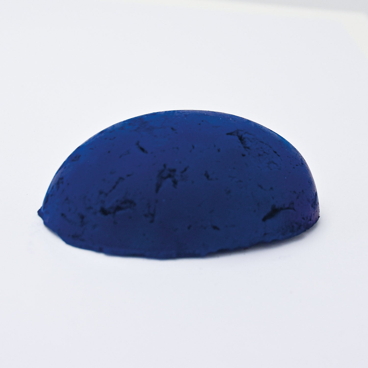 A half egg shaped pastel in a deep cool blue tone, sitting on a white background