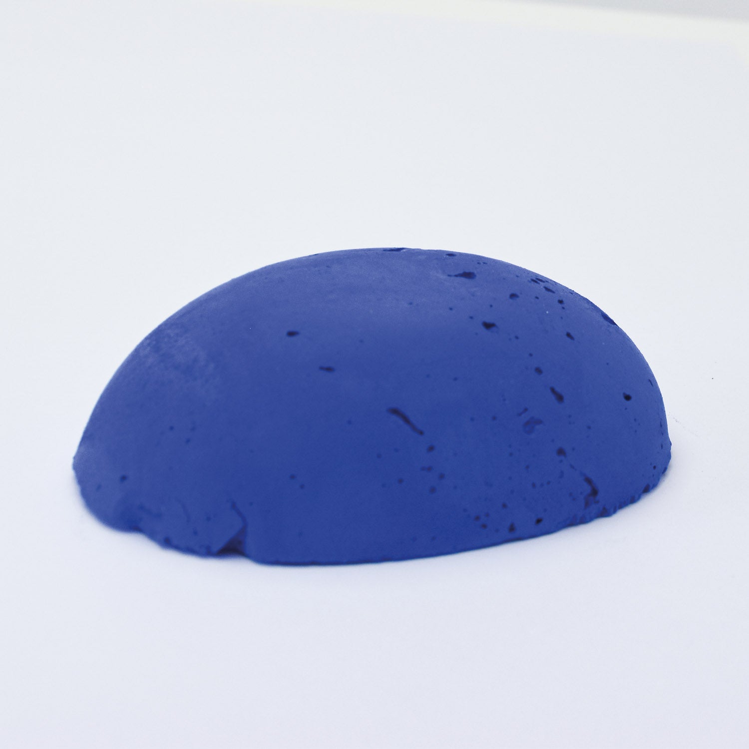 A half egg shaped pastel in a bright blue tone, sitting on a white background