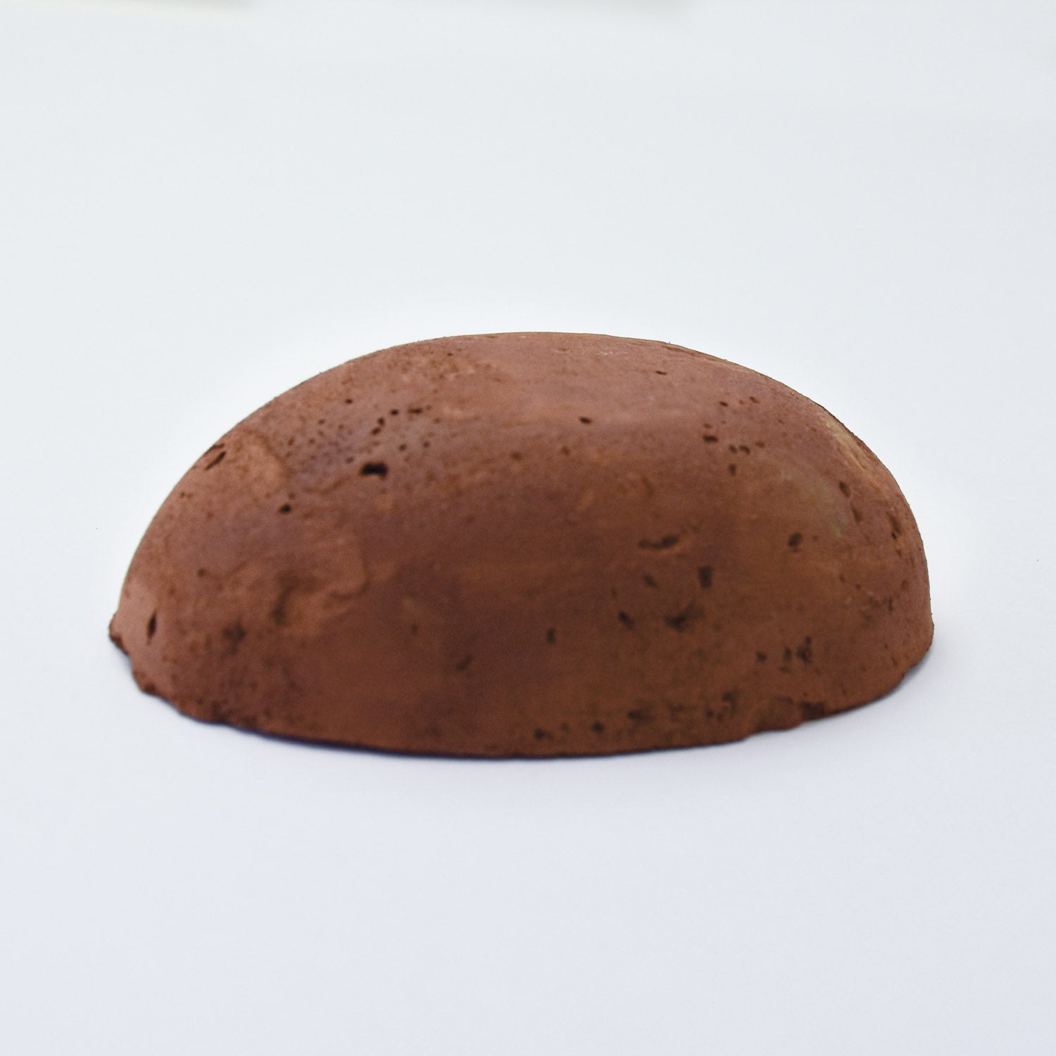 A half egg shaped pastel in a mid-brown tone, sitting on a white background
