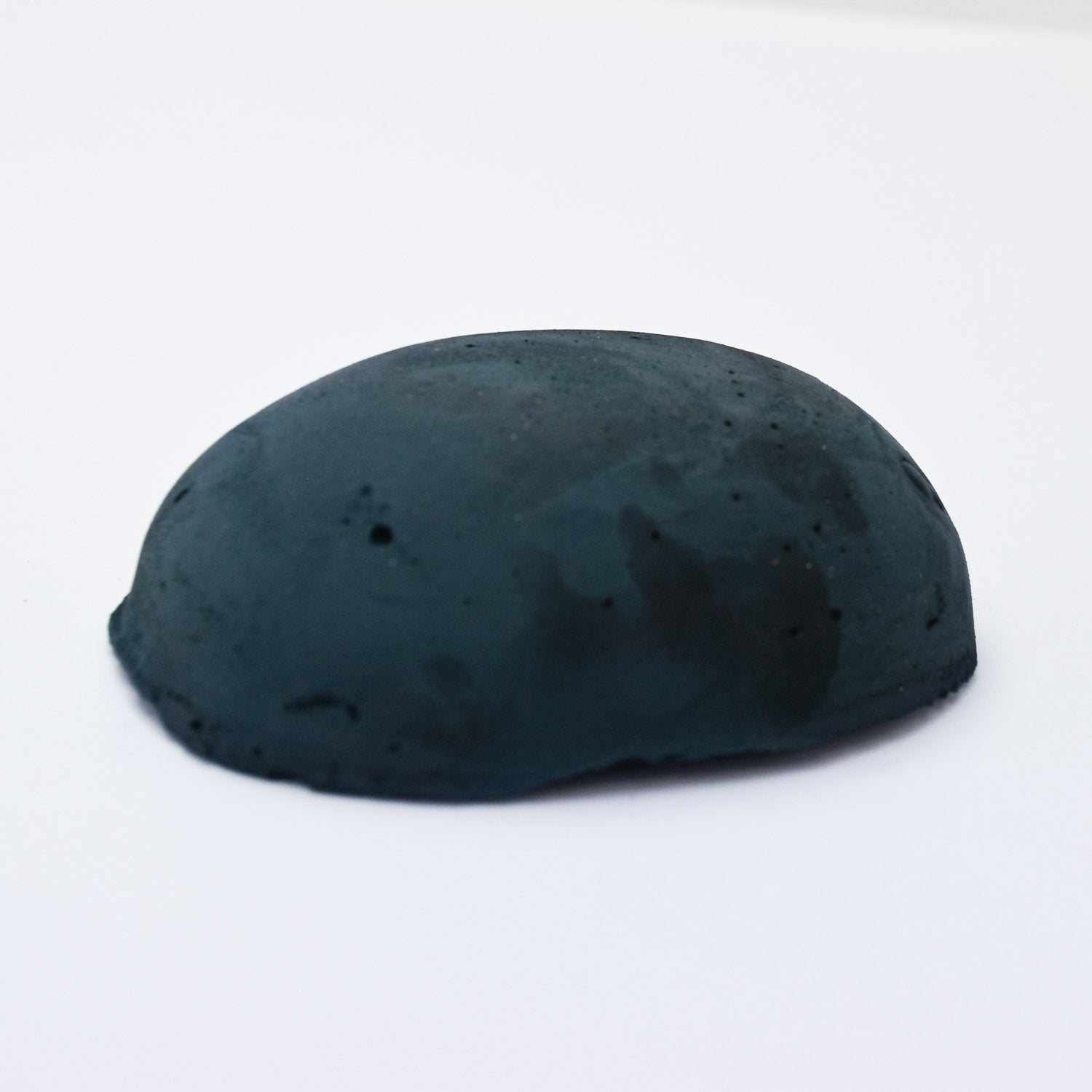 A half egg shaped pastel in a dark blue-green tone, sitting on a white background