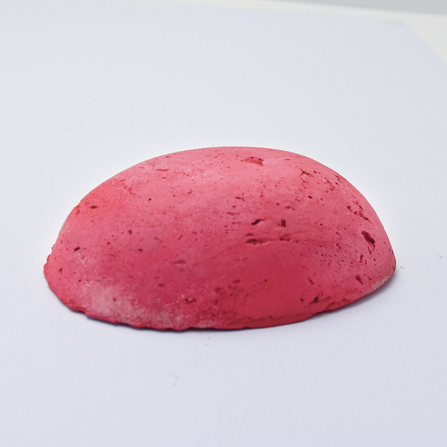 A half egg shaped pastel in a bright pink-red tone, sitting on a white background