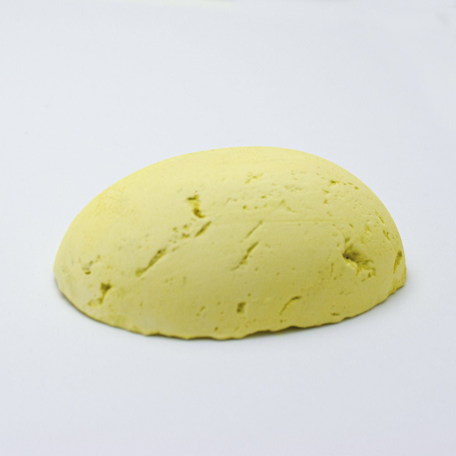 A half egg shaped pastel in a light yellow tone, sitting on a white background