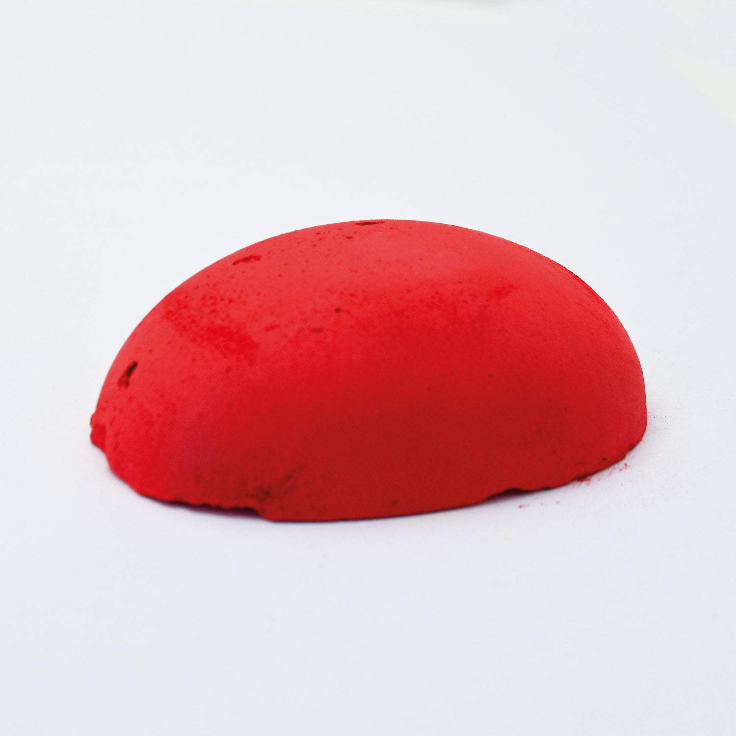 A half egg shaped pastel in an intense red tone, sitting on a white background