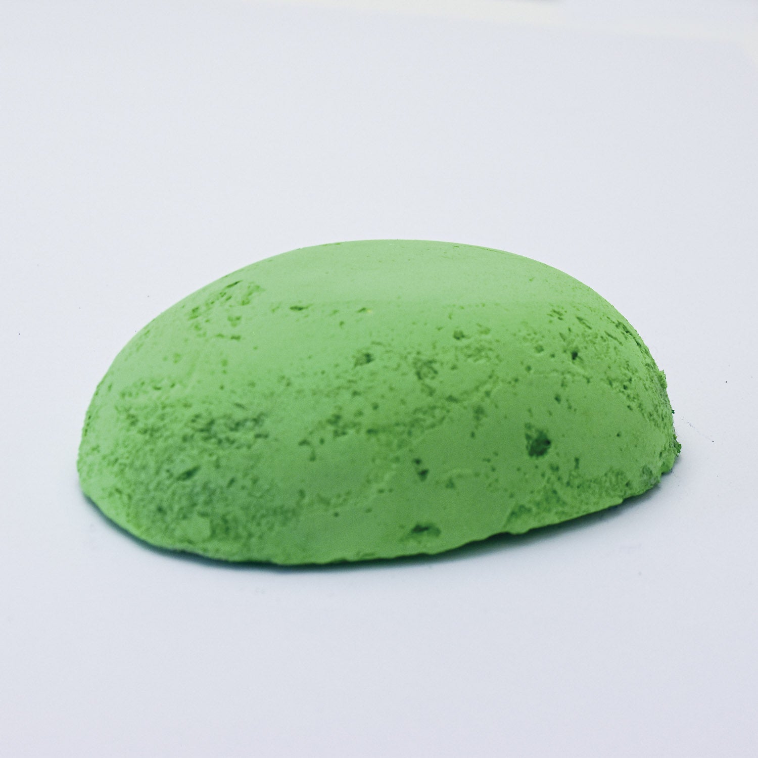 
A half egg shaped pastel in a bright green tone, sitting on a white background
