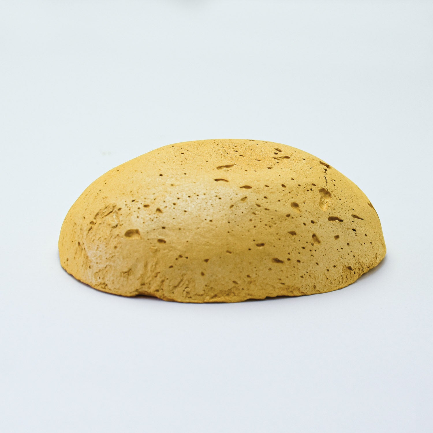 
A half egg shaped pastel in an iridescent yellow ochre tone, sitting on a white background
