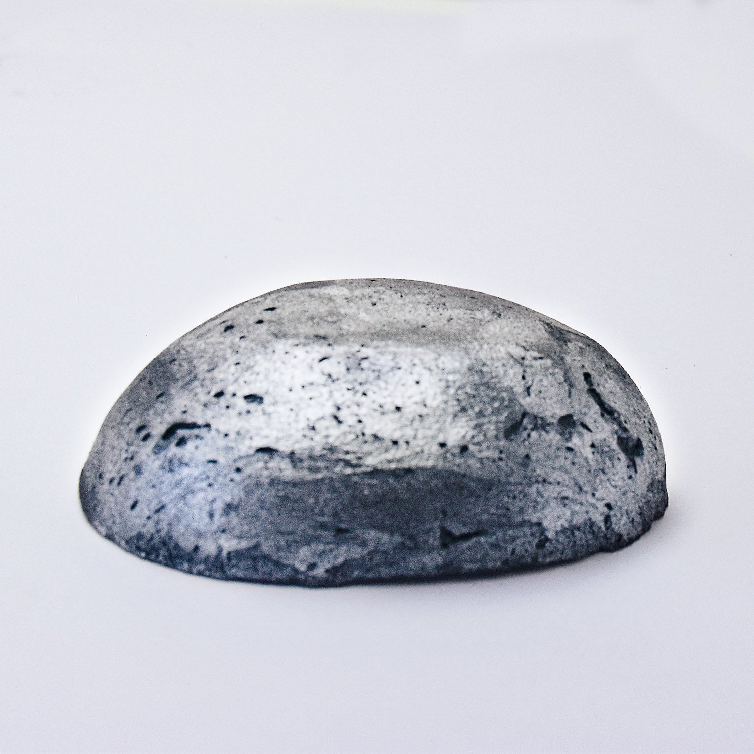 A half egg shaped pastel in a graphite tone, sitting on a white background