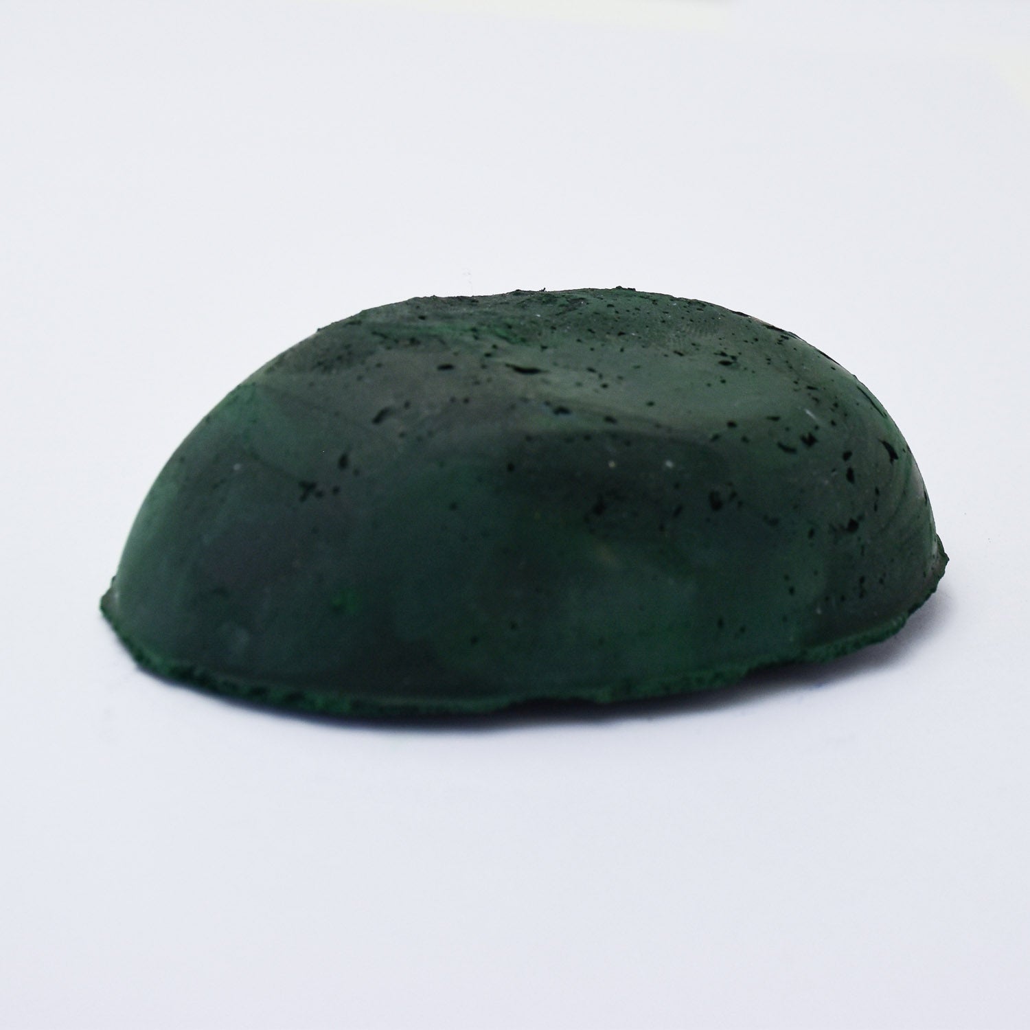 A half egg shaped pastel in a dark green tone, sitting on a white background