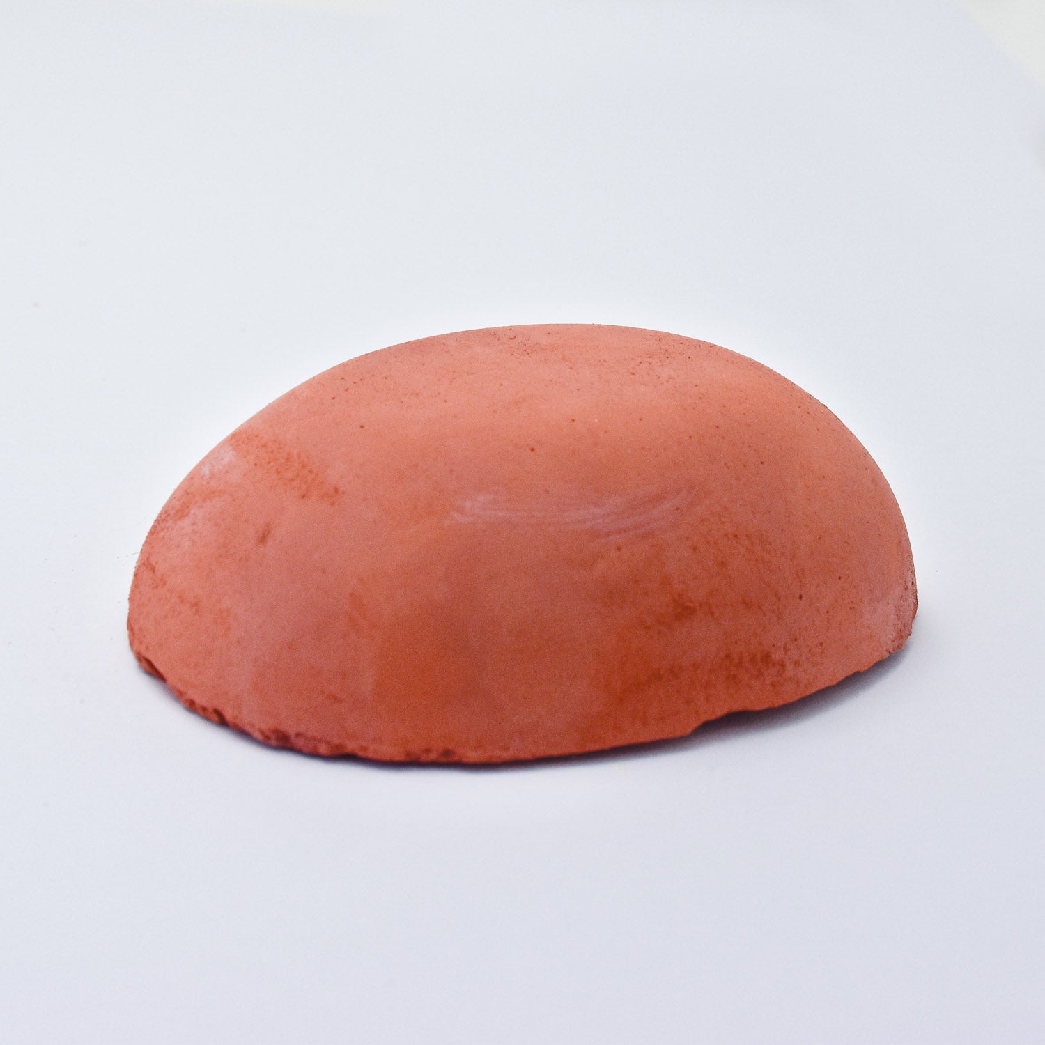 A half egg shaped pastel in a rusty red  tone, sitting on a white background