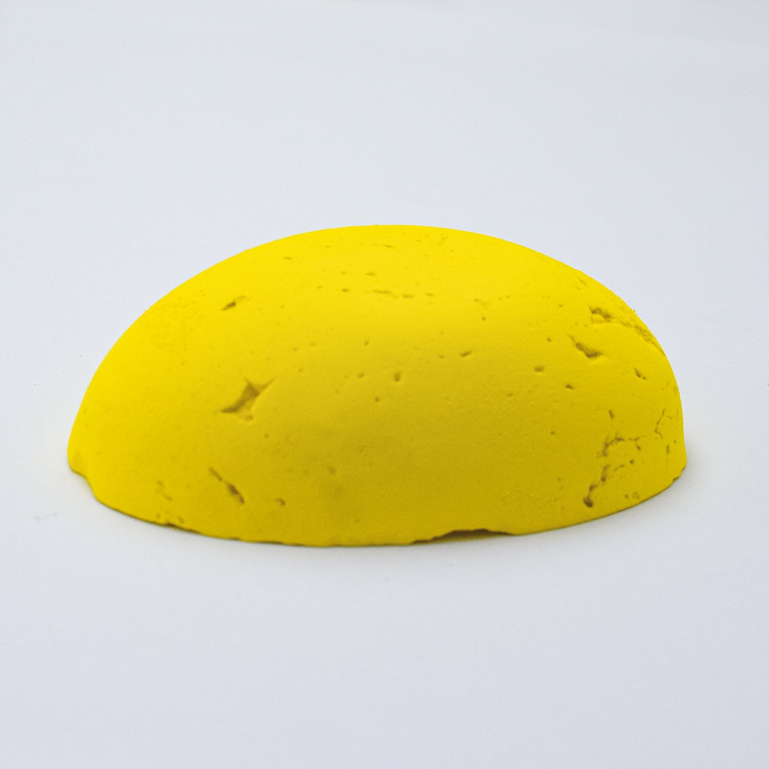 A half egg shaped pastel in a bright yellow  tone, sitting on a white background