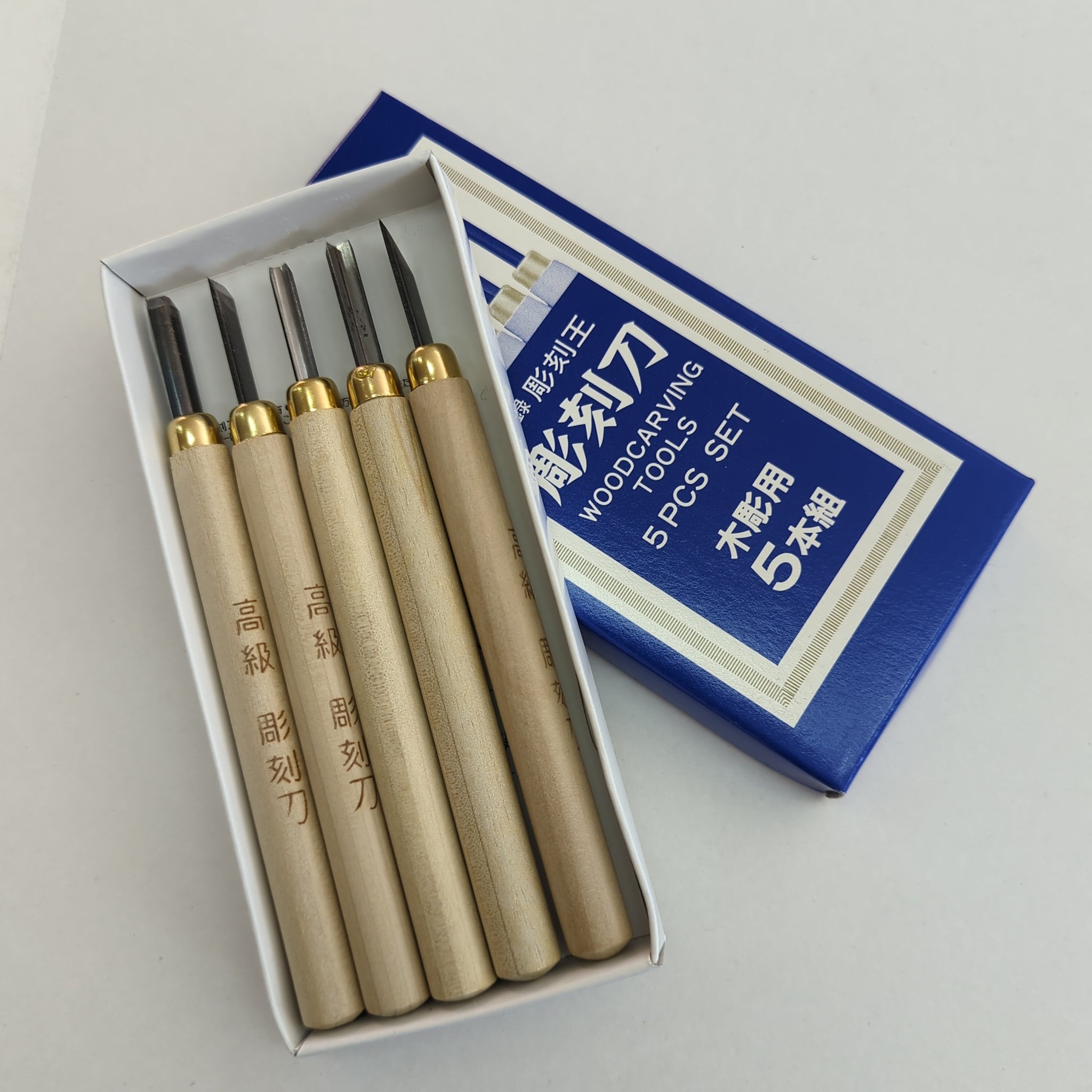 A set of five woodcutting tools with wooden handles and steel blades, presented in an open box with a blue and white lining.