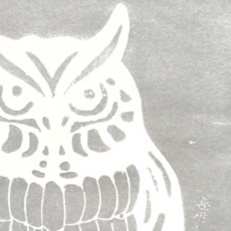 A printed linocut of an owl in silver ink with the outline of the owl appearing in white.
