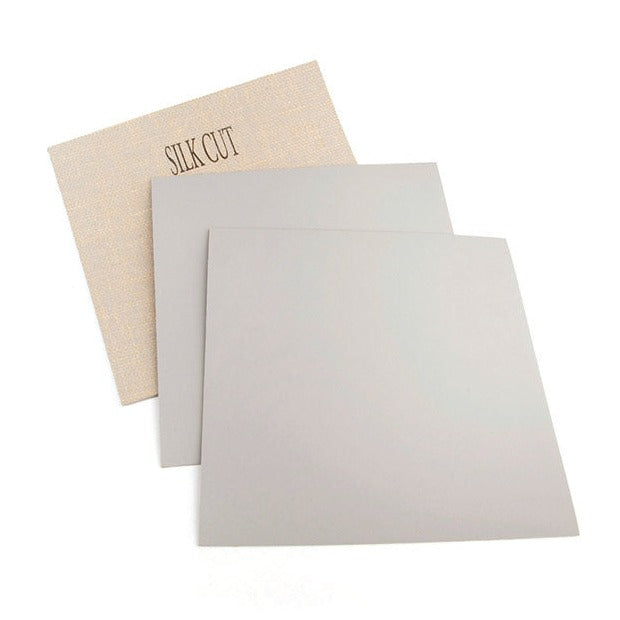 3 sheets of silk cut lino on a white background with 2 showing the grey coloured front and 1 showing the fabric backing and the words Silk Cut printed on it.